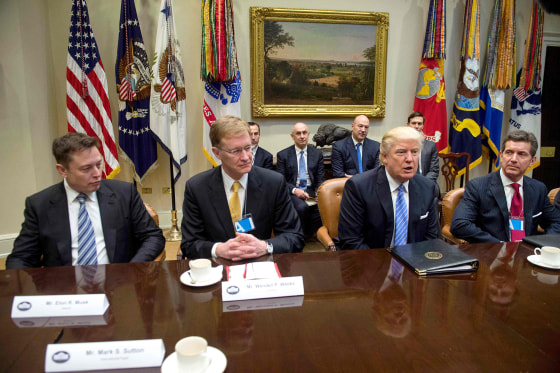 trump sitting at boardroom table leading like a CEO with american flag behind him