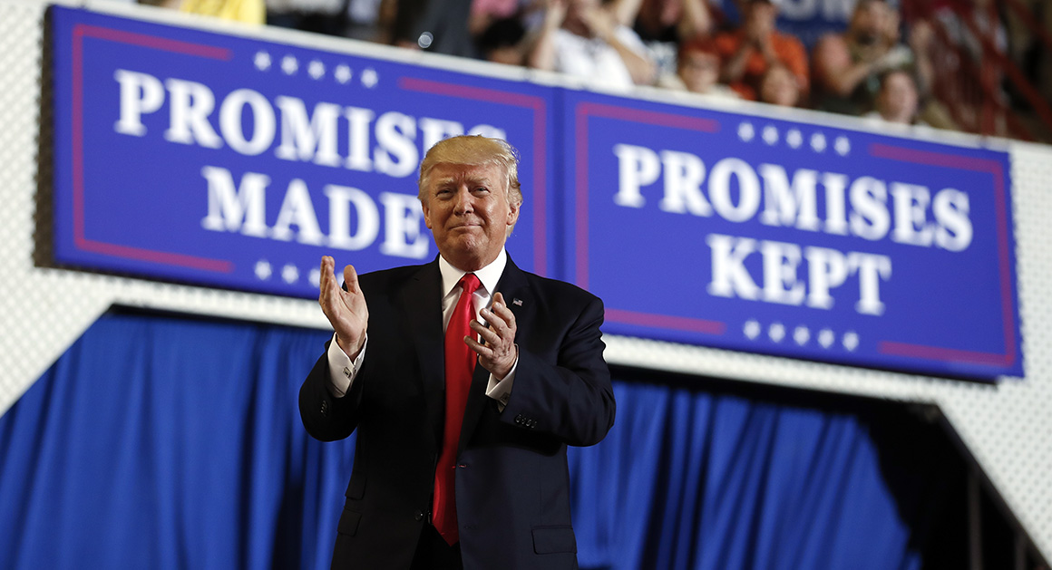 president trump speaking to crowd with large american flag and sign reading “promises made, promises kept”