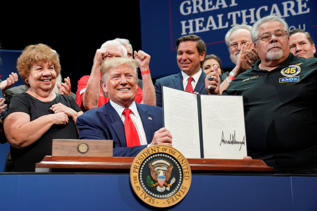 donald trump signing executive order with seniors standing behind him