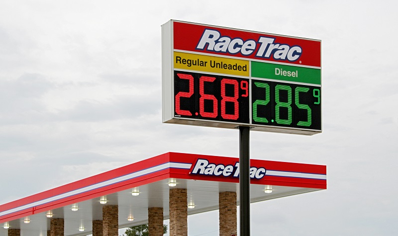 gas station sign showing low fuel prices with cars pumping gas