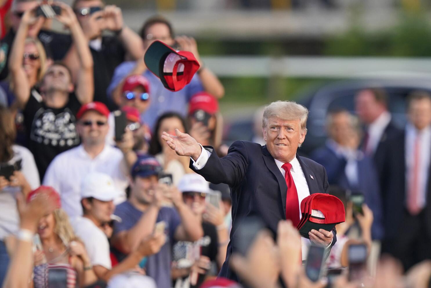 donald trump on stage pointing to crowd wearing red hats and holding trump signs