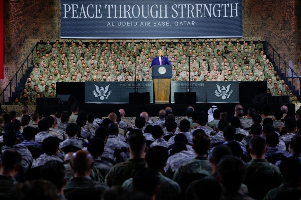 trump holding speech to us military with 'peace throuhg strength' banner behind him