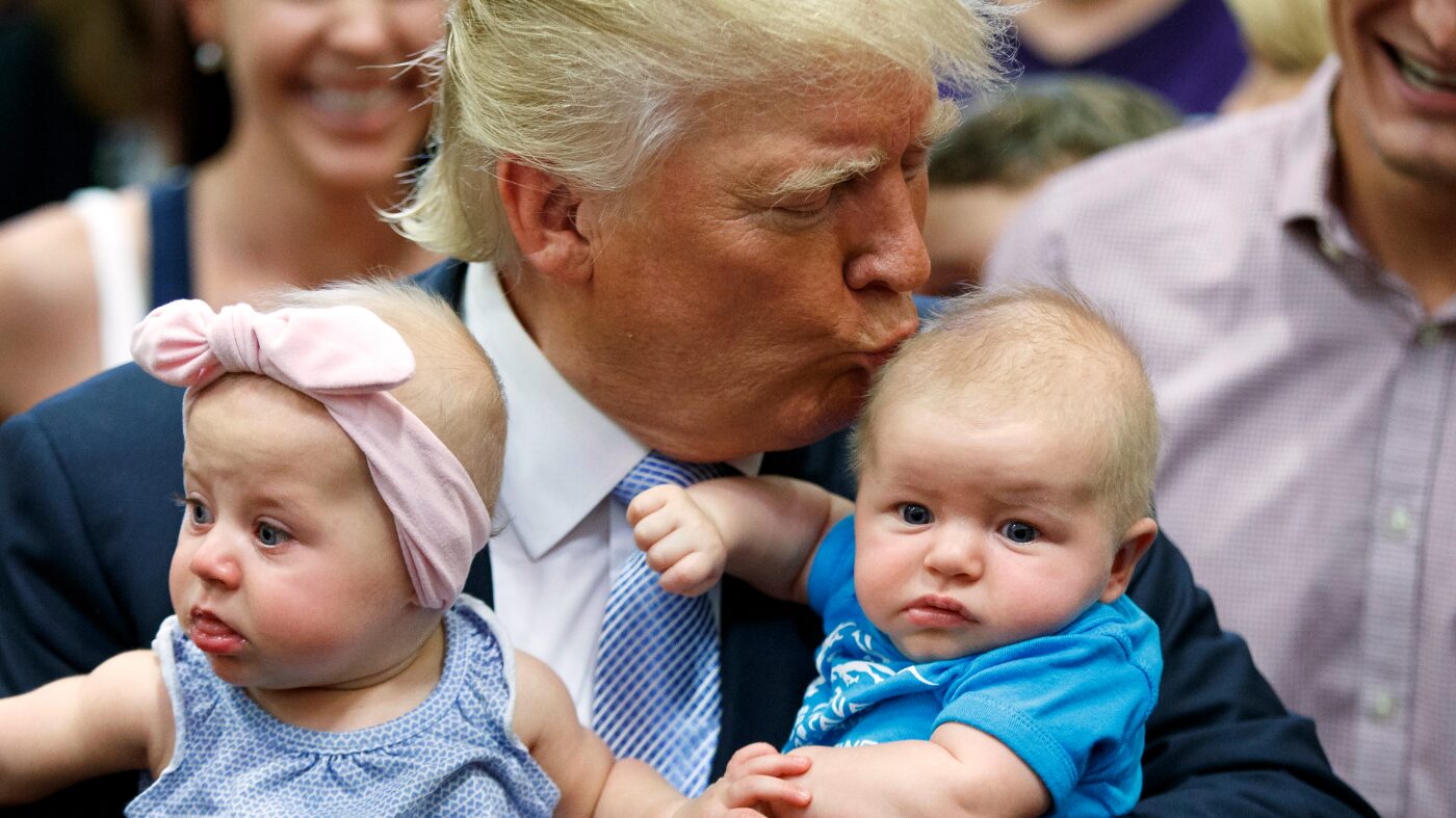 trump with two babies on his arm, giving one a fatherly kiss