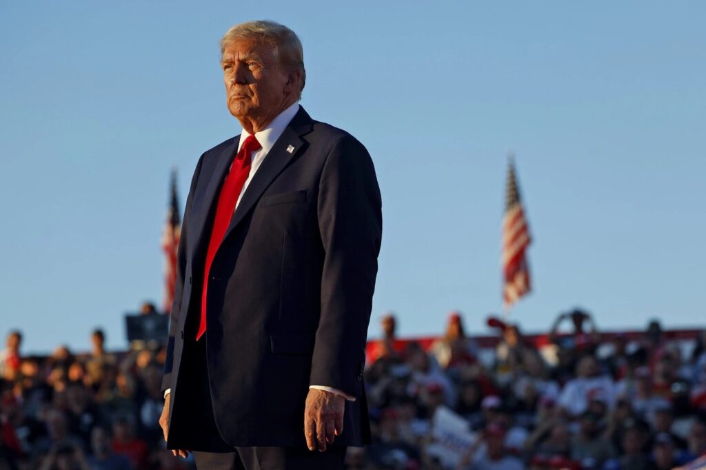trump standing tall at rally wiht american flag in background