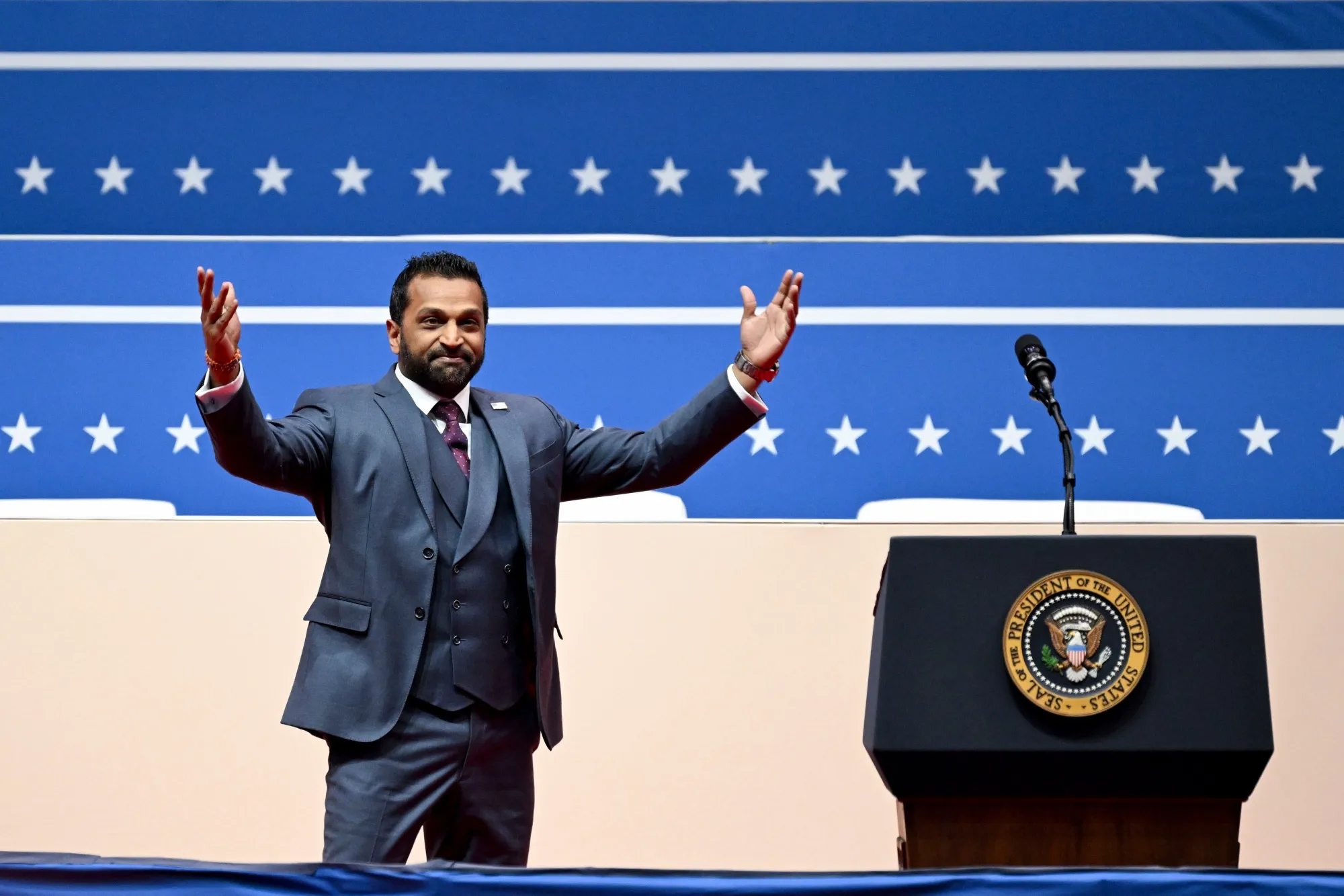 Kash Patel speaking at the DOJ podium with an American flag behind him