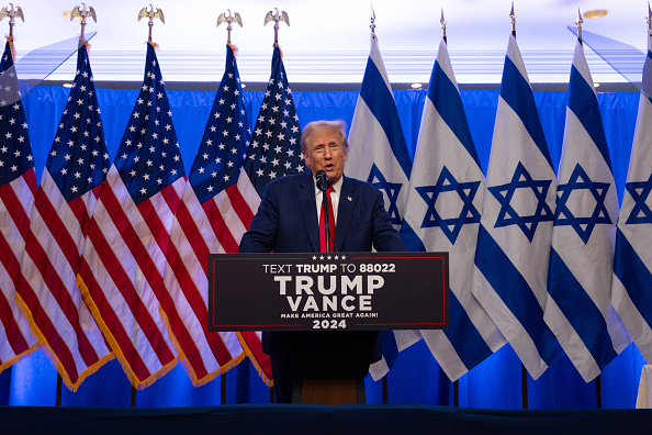 President Donald Trump at a formal event, with a backdrop of American and  Israeli flag